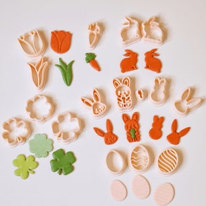 May include: A set of 20 cookie cutters in various shapes, including bunnies, carrots, flowers, clover leaves, and eggs. The cutters are made of white plastic and are arranged on a white surface.