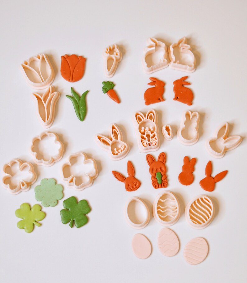 May include: A set of 20 cookie cutters in various shapes, including bunnies, carrots, flowers, clover leaves, and eggs. The cutters are made of white plastic and are arranged on a white surface.