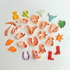 May include: A set of 19 colorful plastic cookie cutters in various shapes, including cowboy boots, horseshoes, cacti, stars, and a money bag. The cutters are arranged in a circle on a white background.