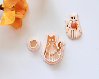 Puede incluir: Tres cortadores de galletas de plástico en forma de un gato sosteniendo una calabaza, un gato y una calabaza. Los cortadores son de color rosa claro.