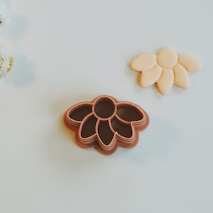 Puede incluir: Dos cortadores de galletas con forma de flor. El cortador más grande es de color marrón claro y el más pequeño es de color marrón oscuro.