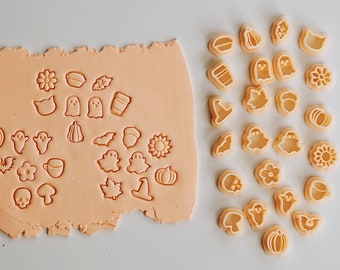 Puede incluir: Un juego de 20 cortadores de galletas en varias formas de otoño y Halloween, incluyendo calabazas, fantasmas, murciélagos, hojas, bellotas y una taza de café. Los cortadores están hechos de plástico beige claro y están dispuestos sobre una superficie blanca.