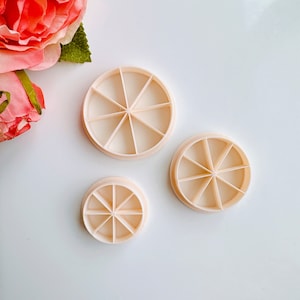 May include: Three round, white plastic cookie cutters with a scalloped edge and a starburst design in the center. The cutters are different sizes.
