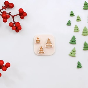 Puede incluir: Un juego de tres cortadores de galletas de árbol de Navidad sobre un fondo blanco. Los cortadores están hechos de plástico y tienen forma de árbol de Navidad. Los cortadores están dispuestos en una fila, con el cortador más grande a la izquierda y el más pequeño a la derecha.