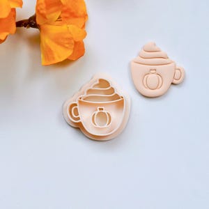 Pode incluir: Um conjunto de dois cortadores de biscoitos de plástico em forma de xícara de café com chantilly e uma abóbora dentro. Os cortadores são de cor pêssego claro.