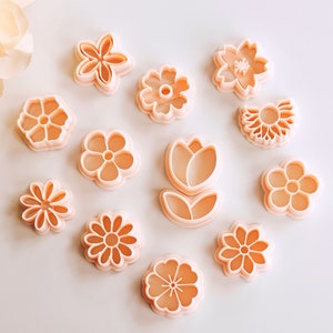 May include: A set of 12 pink plastic flower cookie cutters. The cutters are arranged in a circle on a white background.
