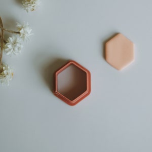 May include: A hexagonal shaped silicone mould with a pink interior and a matching pink lid. The mould is on a white surface.