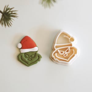 May include: Green and red cookie cutter shaped like the Grinch wearing a Santa hat.