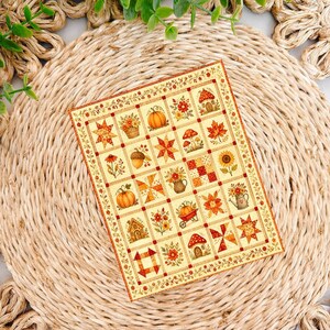 May include: A rectangular card featuring a grid of autumn-themed illustrations including pumpkins, sunflowers, mushrooms, acorns, and maple leaves in shades of orange, yellow, and brown, all framed by a decorative border with small floral motifs.