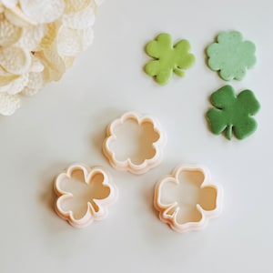 Può includere: Quattro stampini per biscotti in plastica a forma di trifoglio a quattro foglie. Due degli stampini sono bianchi e due sono verdi.