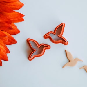 May include: Two red plastic hummingbird cookie cutters and two brown sugar cookie cutouts of hummingbirds.