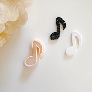 Könnte beinhalten: Drei Musiknotenformen, eine ist weiß, eine ist schwarz mit Glitzer und eine ist ein rosa Plastik-Ausstecher.