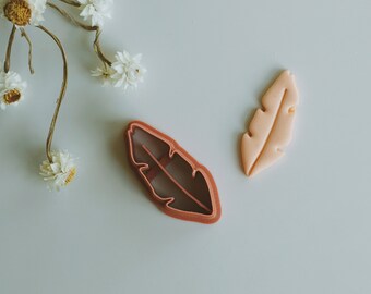 May include: Two cookie cutters in the shape of a leaf. One is a light pink leaf and the other is a brown leaf cutter.