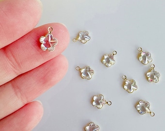 May include: Ten clear crystal flower charms with gold-tone jump rings. The charms are faceted and have a rainbow iridescent finish.