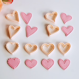 Op de afbeelding: Een set van 12 hartvormige koekjesuitstekers, inclusief zowel gladde als gegolfde randen. De uitstekers zijn gemaakt van wit plastic en zijn verkrijgbaar in verschillende maten.