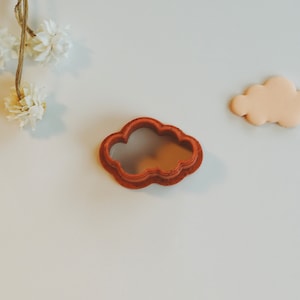 Puede incluir: Un cortador de galletas en forma de nube de plástico marrón sobre un fondo blanco.