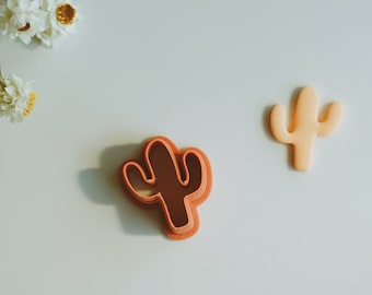 Peut inclure: Deux emportes-pièces en forme de cactus, l'un est de couleur orange clair et l'autre est de couleur orange foncé. Les emportes-pièces sont sur une surface blanche.