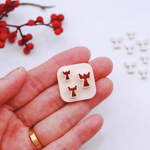 May include: A white plastic mould with three small, detailed angel shapes. The mould is being held in a person's hand.