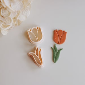 May include: Three cookie cutters in the shape of tulips. One is a light pink, one is a light green, and one is a light orange.
