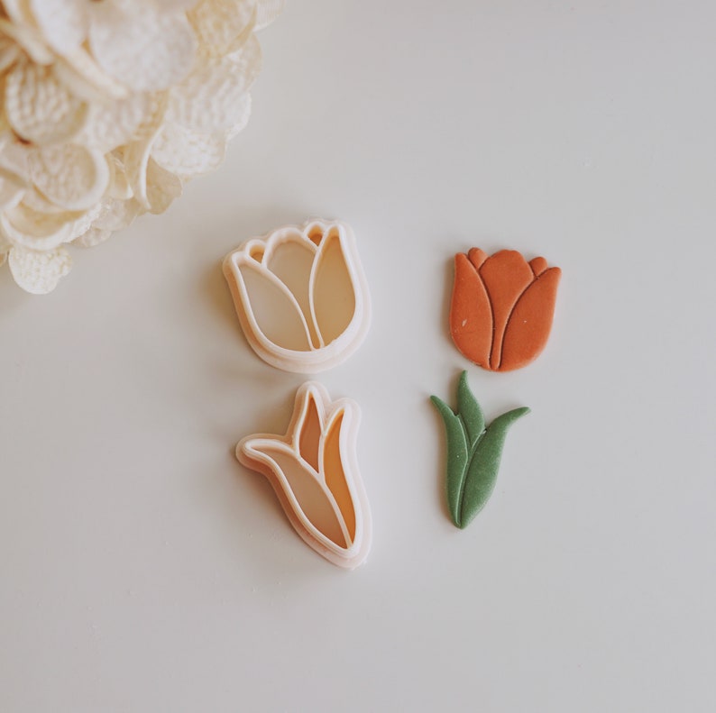 May include: Three cookie cutters in the shape of tulips. One is a light pink, one is a light green, and one is a light orange.