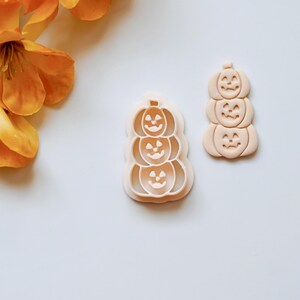 Puede incluir: Un juego de dos cortadores de galletas de pl&aacute;stico con forma de pila de tres calabazas con caras de calabaza. Los cortadores son de color beige claro.
