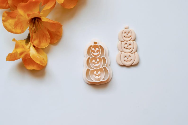 Puede incluir: Un juego de dos cortadores de galletas de pl&aacute;stico con forma de pila de tres calabazas con caras de calabaza. Los cortadores son de color beige claro.