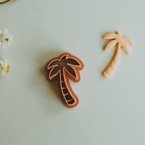 Puede incluir: Dos cortadores de galletas con forma de palmera, uno es de color naranja claro y el otro es de color naranja oscuro. Ambos tienen un diseño detallado.