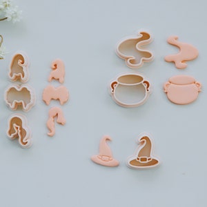 May include: A set of 10 pink plastic cookie cutters in various shapes, including a cauldron, a witch's hat, and flames. The cutters are designed for making Halloween-themed cookies.