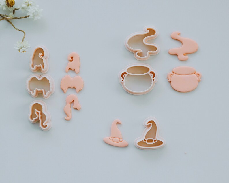 May include: A set of 10 pink plastic cookie cutters in various shapes, including a cauldron, a witch's hat, and flames. The cutters are designed for making Halloween-themed cookies.