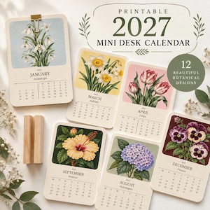 May include: A 2027 mini desk calendar set featuring 12 botanical designs. Each card displays a month, a flower illustration, and a calendar grid. The set includes a wooden stand and cards for January, March, April, August, September, and December.