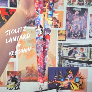 May include: A colorful lanyard and matching keychain featuring a repeating pattern of cartoon characters in red, blue, and purple. The lanyard has a metal clasp and the text "STOLITZ LANYARD + KEYCHAIN".