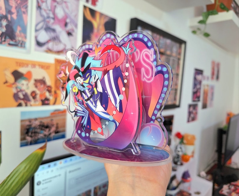 May include: A colorful acrylic stand featuring a cartoon character with a black and white striped suit, a red and blue cape, and a blue and white jester hat. The stand has a pink and purple background with a neon sign that says "VIP's".