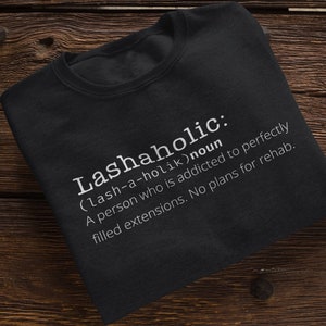 May include: Black t-shirt with white text that reads "Lashaholic: (lash-a-holik) noun A person who is addicted to perfectly filled extensions. No plans for rehab."