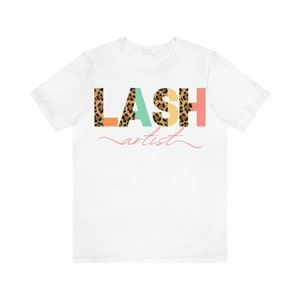 May include: White t-shirt with the text "LASH artist" in colorful letters. The letters are decorated with a leopard print pattern.