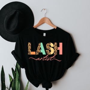 May include: Black t-shirt with the text "LASH artist" in colorful letters with a leopard print pattern.