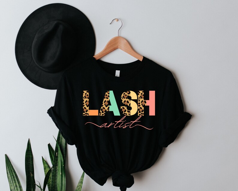 May include: Black t-shirt with the text "LASH artist" in colorful letters with a leopard print pattern.