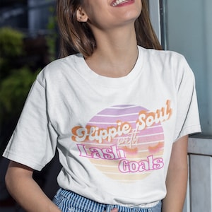 Puede incluir: Camiseta blanca con un gr&aacute;fico rosa y naranja que dice "Hippie Soul with Lash Goals".
