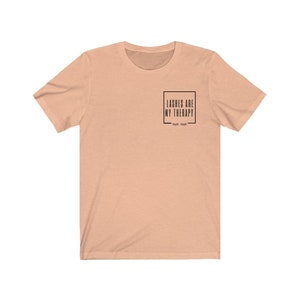May include: A peach coloured t-shirt with the text "Lashes are my therapy" in a black box with eyelashes underneath.