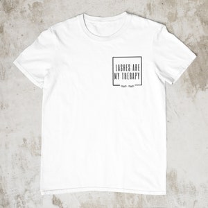 May include: White t-shirt with a black square graphic that says "Lashes are my therapy" with a pair of eyelashes underneath.