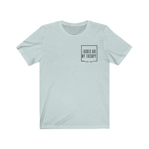 May include: A light blue t-shirt with the text "Lashes are my therapy" in a black box with eyelashes underneath.