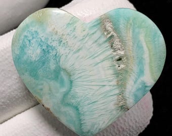 May include: A heart-shaped polished stone with a white and blue swirling pattern. The stone has a light blue colour with white veins and a white centre.