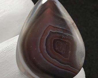 以下が含まれることがあります： 茶色、灰色、白の渦巻き模様が施された、涙滴型の瑪瑙カボション。石は滑らかで磨かれた表面をしています。