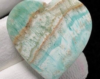 May include: A heart-shaped piece of polished aquamarine with white and brown veins. The stone has a light blue colour and a smooth, polished surface.