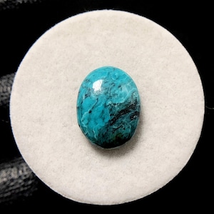 Peut inclure: Pierre précieuse ovale, d'un bleu turquoise vif, avec des motifs sombres et tourbillonnants. La pierre polie repose sur une surface circulaire blanche, sur fond noir. Idéale pour la création de bijoux.