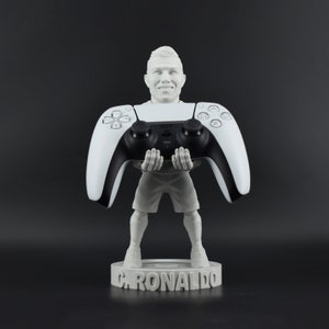 Peut inclure: Figurines blanche d'une personne tenant une manette de jeu vidéo noire et blanche. La base de la figurine porte le nom "C. RONALDO".