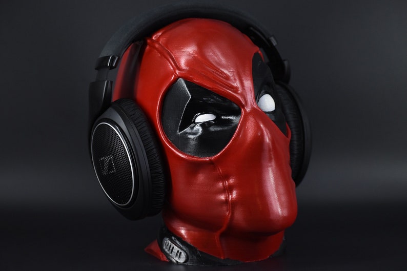 May include: Black over-ear headphones with a silver accent on the earcups are worn by a red and black Deadpool mask.