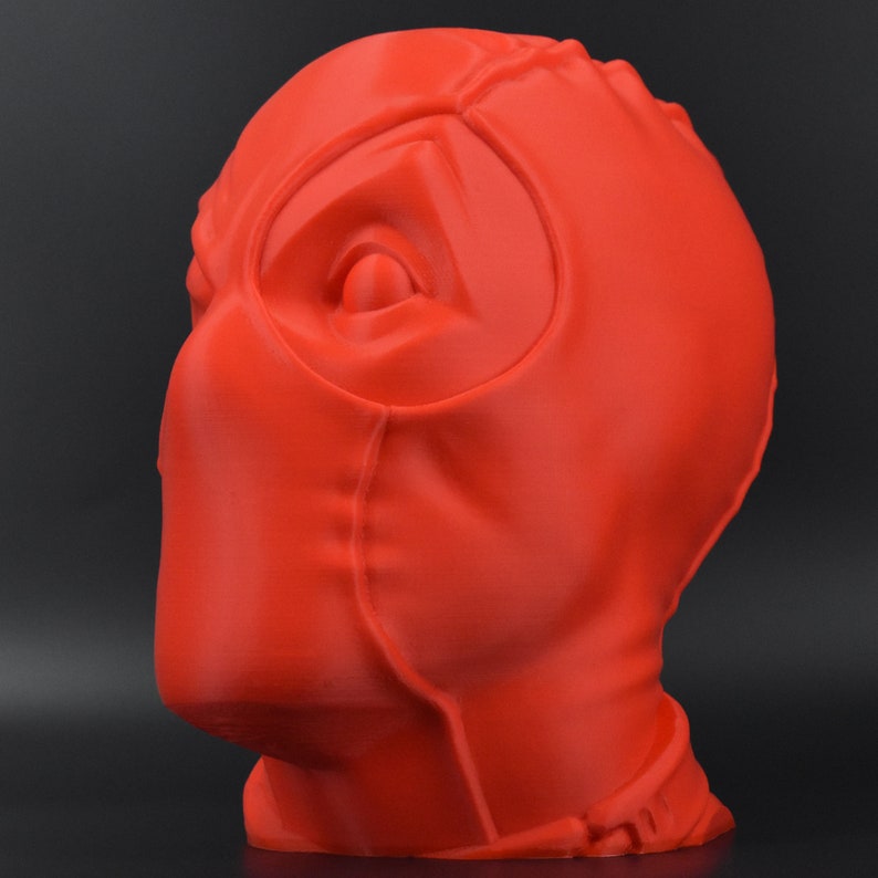 May include: A red 3D printed bust of Deadpool's head. The bust is detailed with a mask and eye holes.