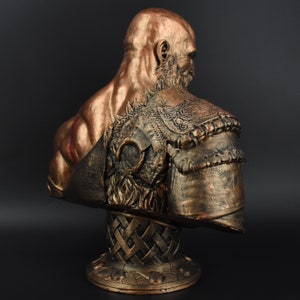 Puede incluir: Un busto de bronce de un guerrero con un dise&ntilde;o detallado, texturizado e intrincado. El busto est&aacute; sobre una base con un patr&oacute;n tejido.