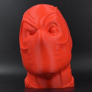 May include: A 3D printed red bust of Deadpool's head. The bust is detailed with a mask and facial features.