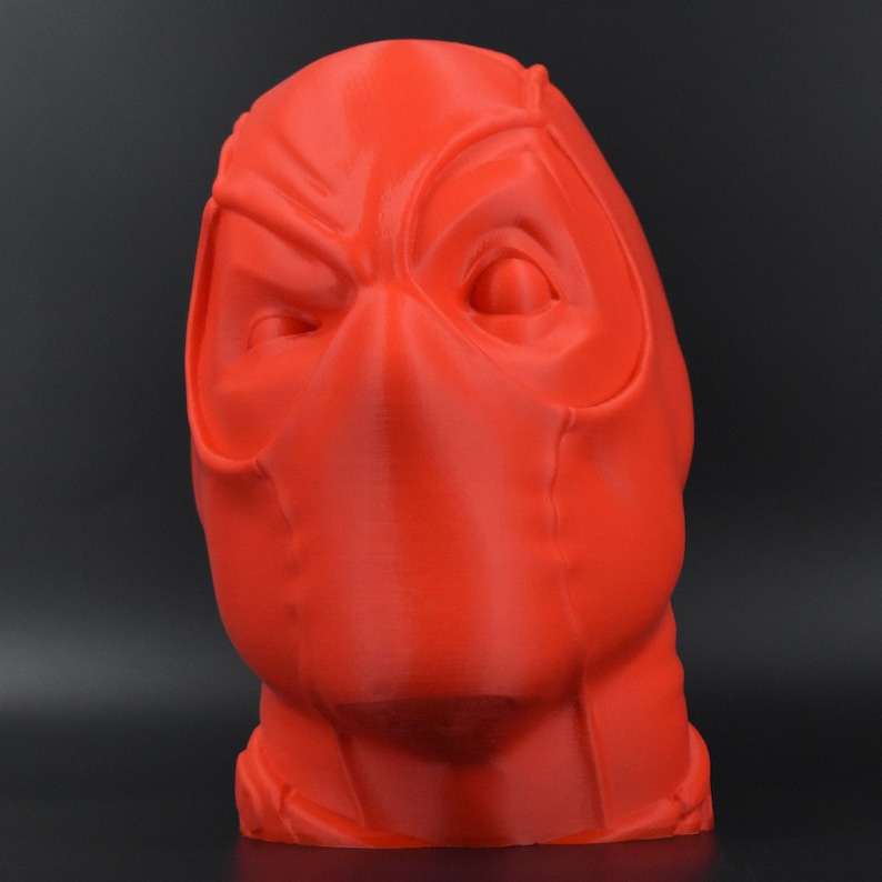 May include: A 3D printed red bust of Deadpool's head. The bust is detailed with a mask and facial features.